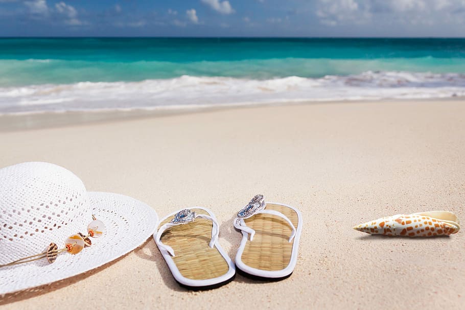 pair of beige-and-white flip-flops beside white hat on seashore during day HD wallpaper