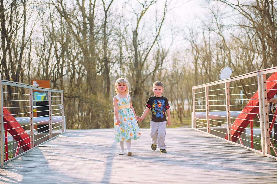 boy and girl holding each others hand while walking on bridge