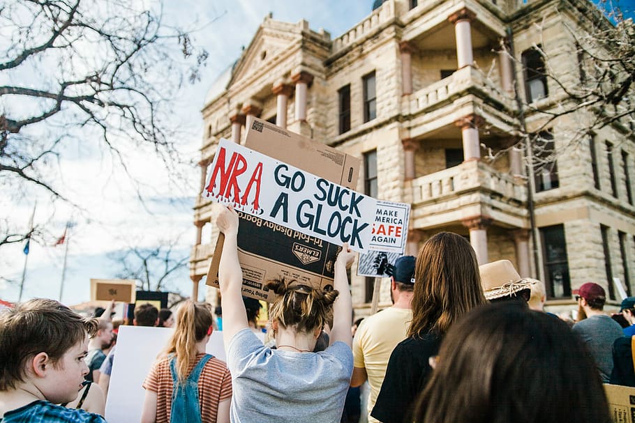 assembly of people front of building, woman showing signage together with people rallying HD wallpaper
