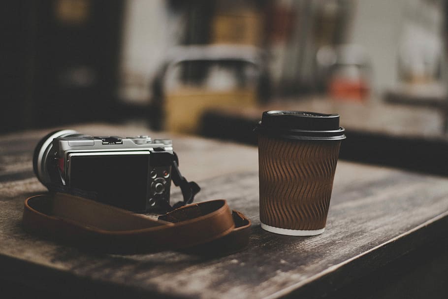gray DSLR camera beside brown plastic cup, gray point-and-shoot camera beside black cup on brown wooden table HD wallpaper