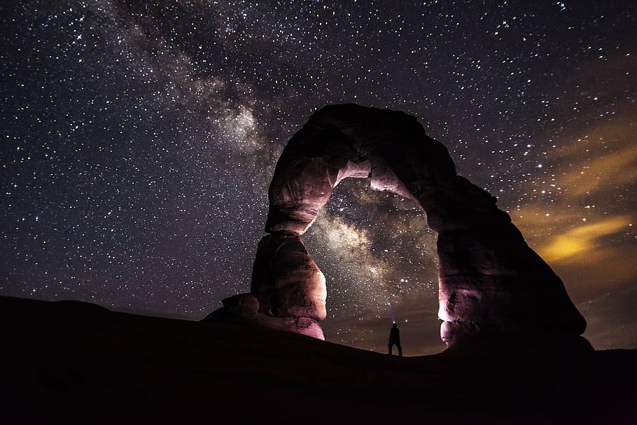 silhouette of man under formation of rock during nighttime, delicate arch