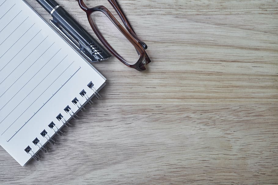 steno notebook beside black pen and brown framed eyeglasses, eyewear