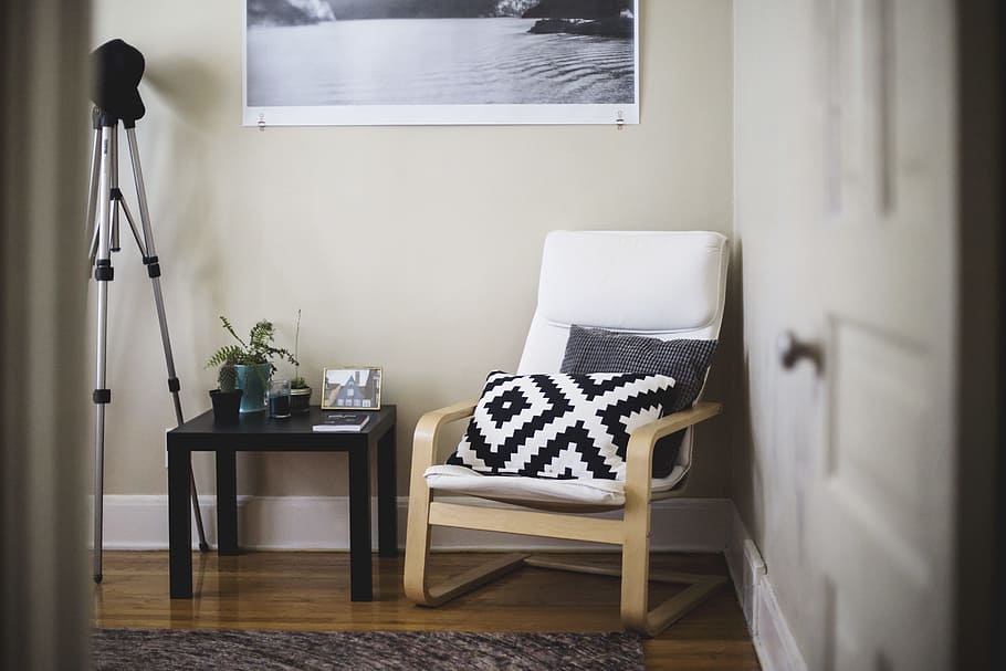 throw pillow on chair beside end table inside room, brown wooden framed white padded chair beside black wooden table with green potted plant