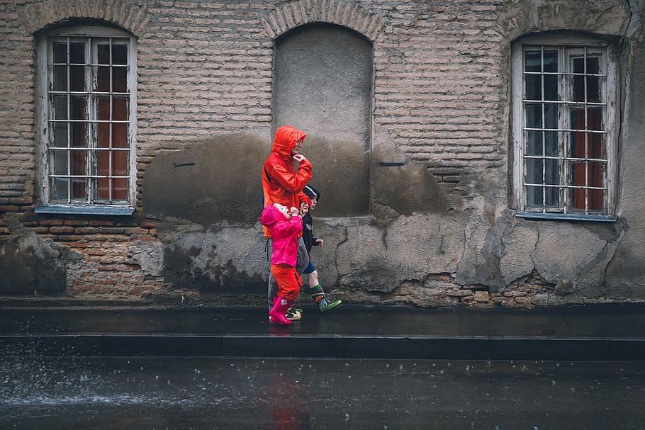 person wearing red rainy coat while with his/her children walking on black asphalt road HD wallpaper