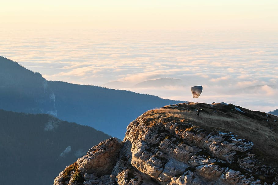 hand glider on top of rock formations near silhouette of mountains under cloud sky HD wallpaper