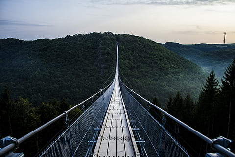 gray and black wooden bridge across mountains covered by trees, bridge during daytime HD wallpaper