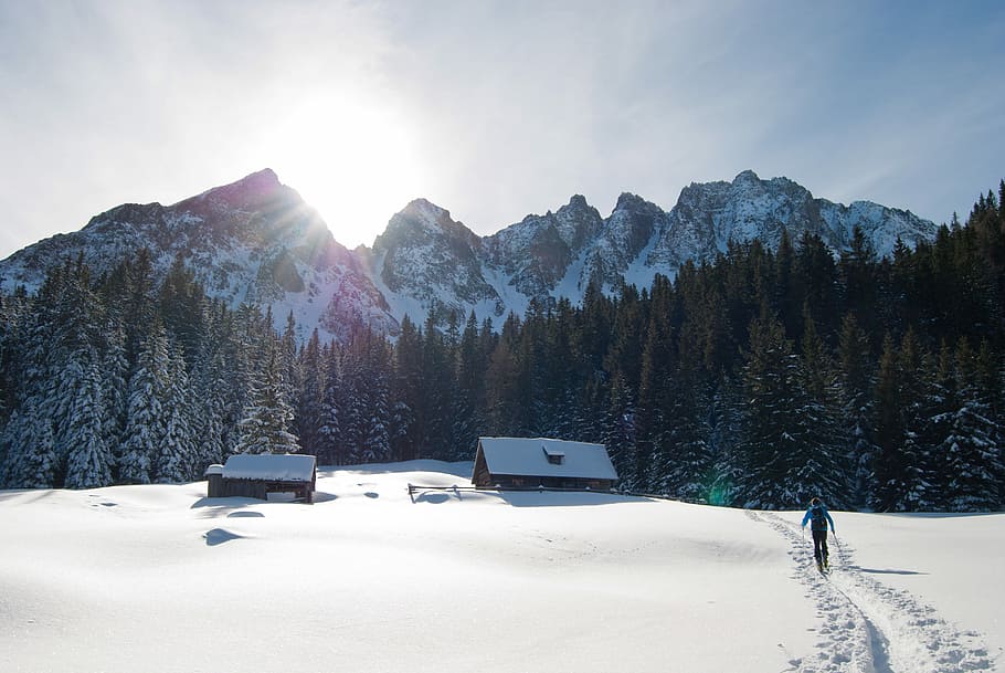 person walking on snowfield near mountain range, person walking on snow field towards cabin HD wallpaper