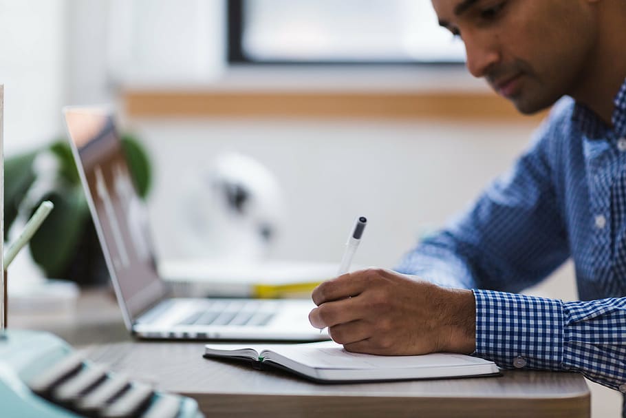 man sitting at desk using laptop while writing, computer, browser HD wallpaper
