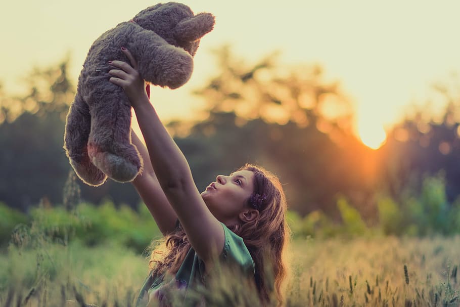 woman with green shirt lifting brown bear plush toy during daytime HD wallpaper