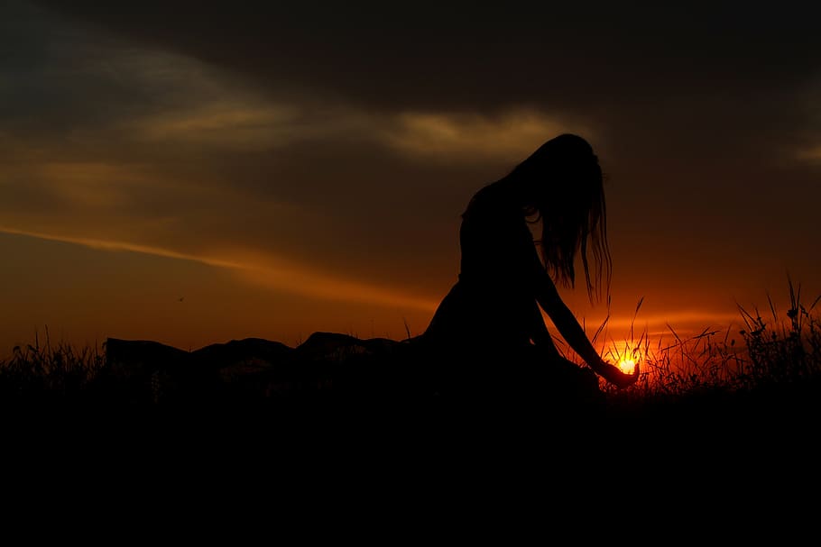 silhouette photography of woman sitting on grass under grey clouds orange skies sunset HD wallpaper