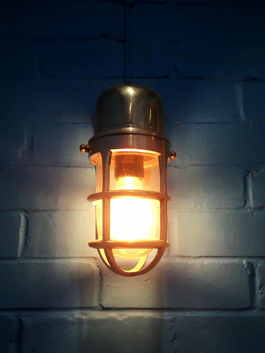 gray turned-on sconce lamp with cage on white wall, light bulb