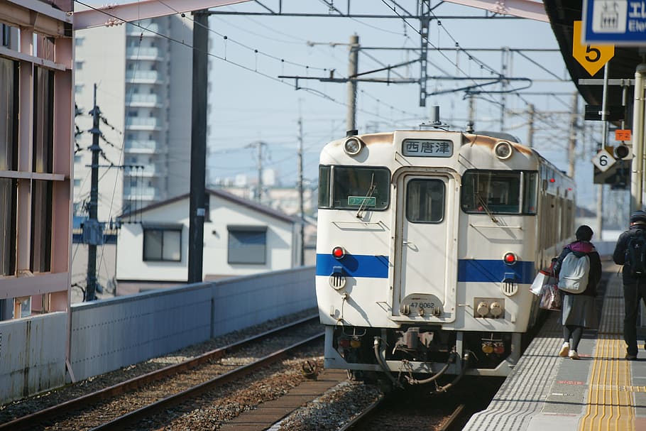 white train passing on subway, two people walking on rail station near white locomotive train HD wallpaper