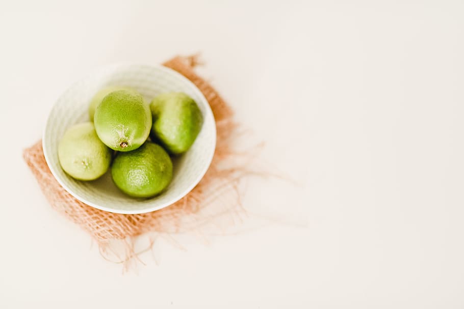 pile of lemon in bowl, round green fruits on white ceramic bowl HD wallpaper