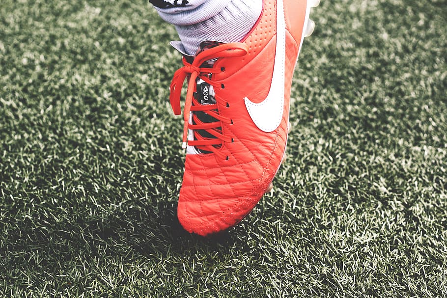 unpaired orange and white Nike soccer cleat, person wearing orange Nike shoe