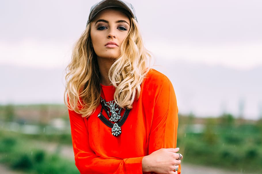 woman in orange crew-neck long-sleeved shirt and blue baseball cap standing photoshoot at daytime, woman in red long-sleeved shirt during daytime, HD wallpaper