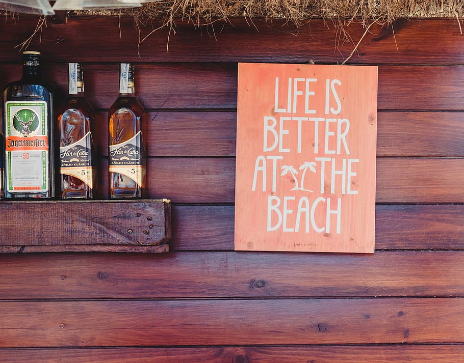 three assorted-brand whiskey bottle, life is better at the beach signage near three liquor bottles