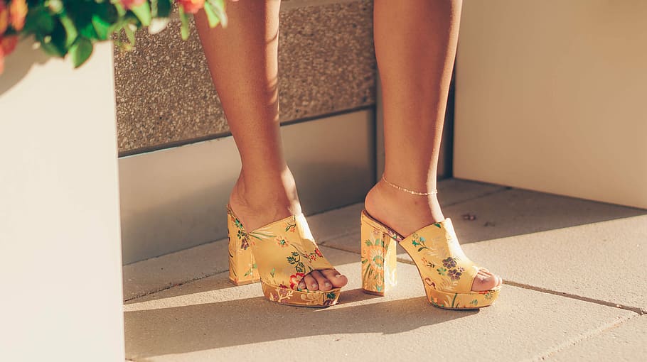 woman wearing yellow sandals standing near brown wall, woman wearing yellow floral open-tie platform chunky heels