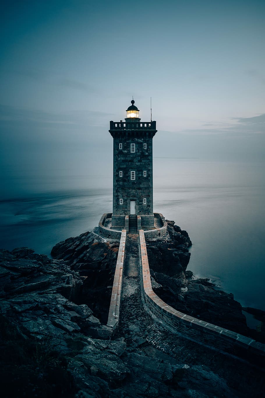gray concrete building on cliff, lighthouse on rocky mountain near body of water HD wallpaper