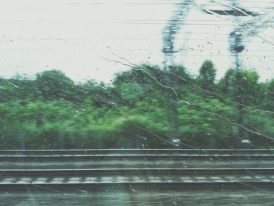 photo of rain drops, water droplets on moving train's window with blurry forest background HD wallpaper