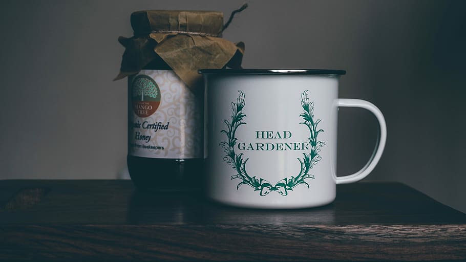 white head gardener ceramic cup near glass jar on brown panel, white and green head gardener ceramic cup beside glass jar HD wallpaper
