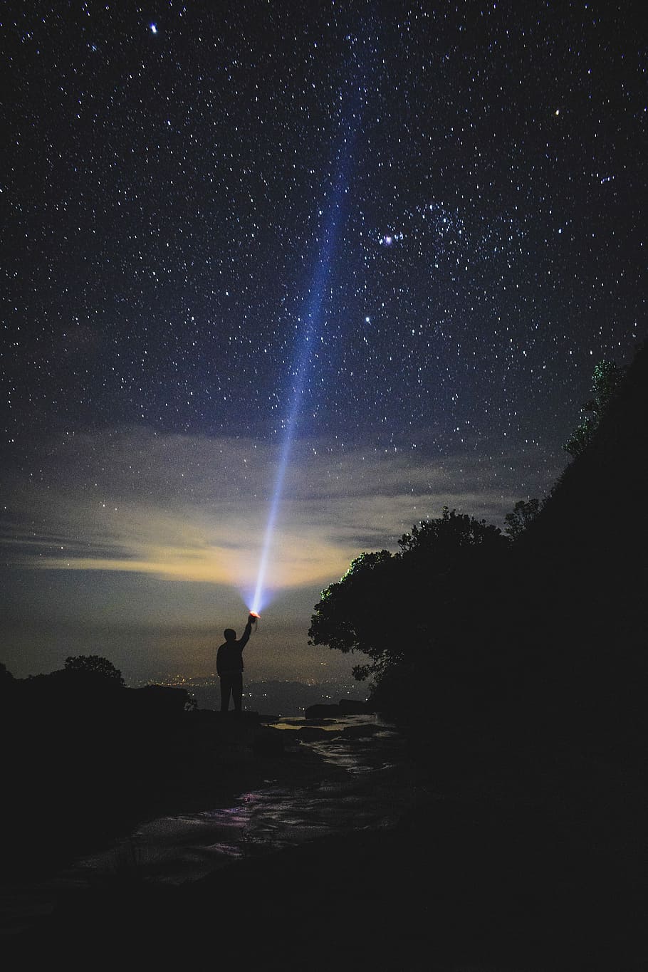 man holding flashlight pointing towards sky, silhouette of person holding torch pointing to sky at night
