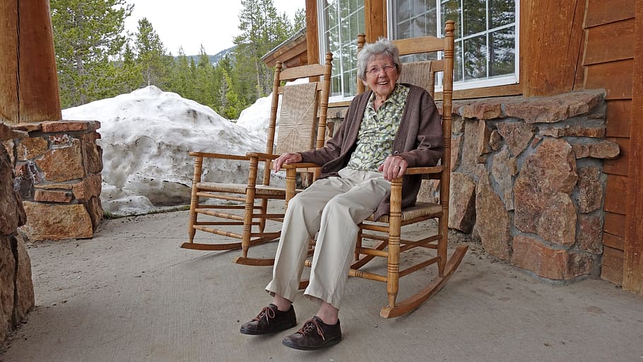 woman in green shirt and gray pants with brown cardigan sitting on brown wooden rocking chair