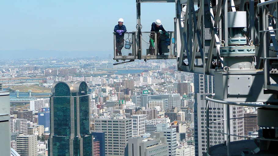 two construction workers standing on crane on top of building HD wallpaper