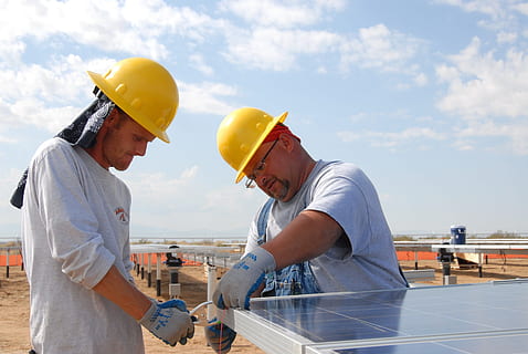 two men in yellow hard hat helmets installing solar panels during daytime HD wallpaper