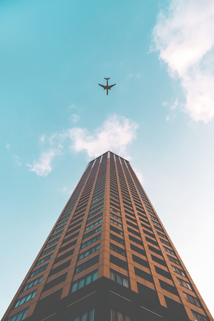 bottom view shot of airplane flying above high rise building, white airliner flying over brown high rise building during daytime