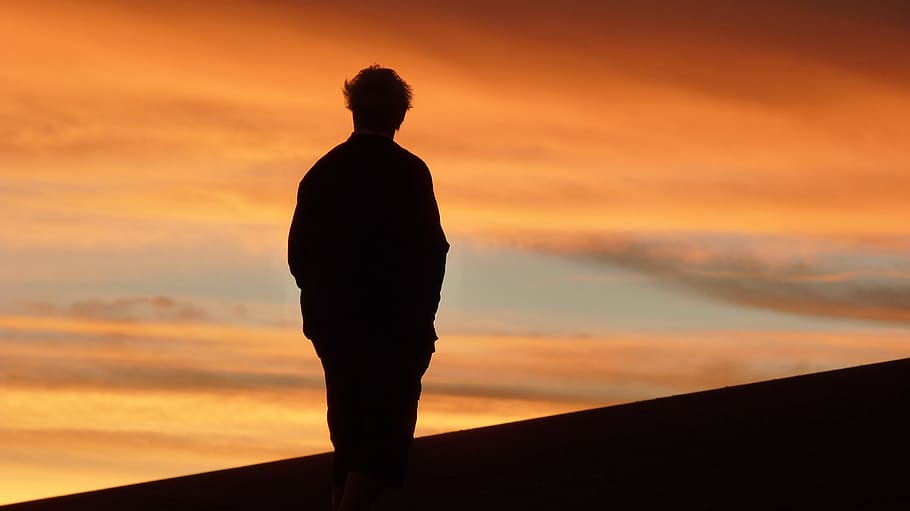 silhouette of person standing on hill during daytime, sunset