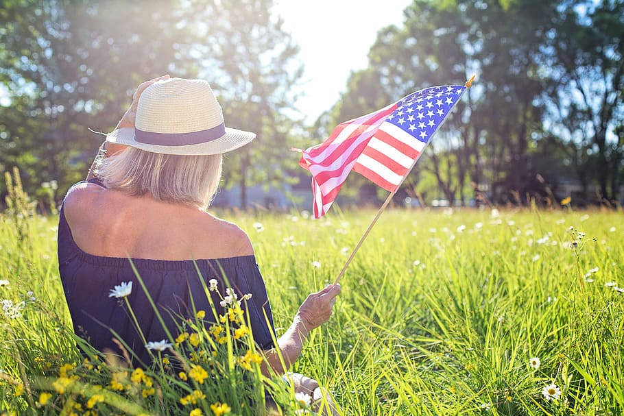 woman holding U.S.A flag sitting on green grass field during daytime
