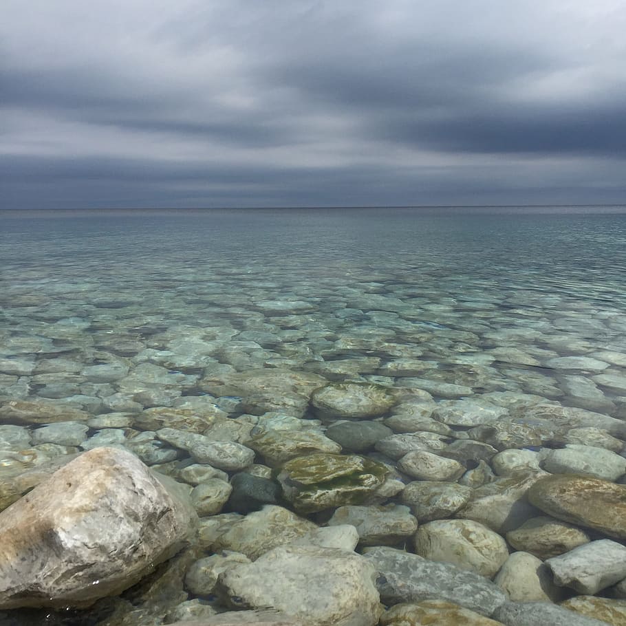 body of water with stones under cloudy sky, sea horizon during cloudy day