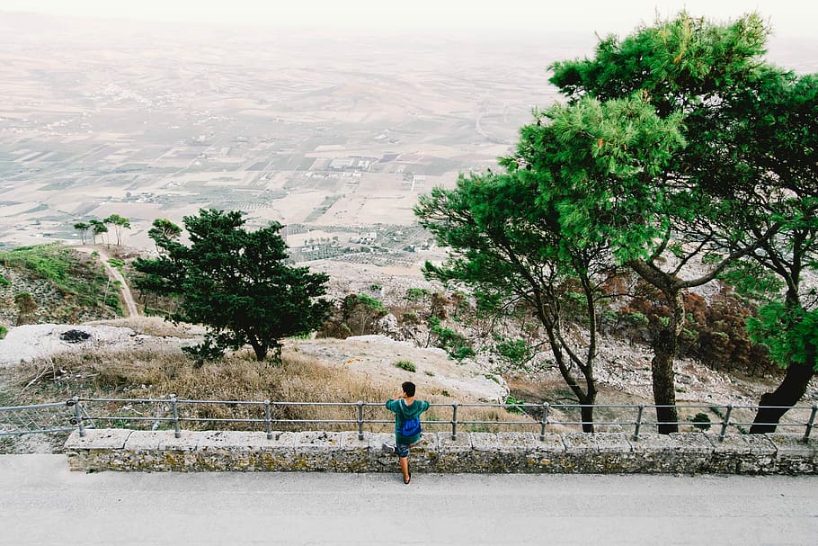 person standing on fence while looking below, person wearing green dress beside gray fence HD wallpaper