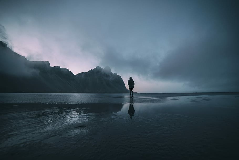 man standing on seashore during daytime, silhouette of man standing on the shore with dark clouds above HD wallpaper