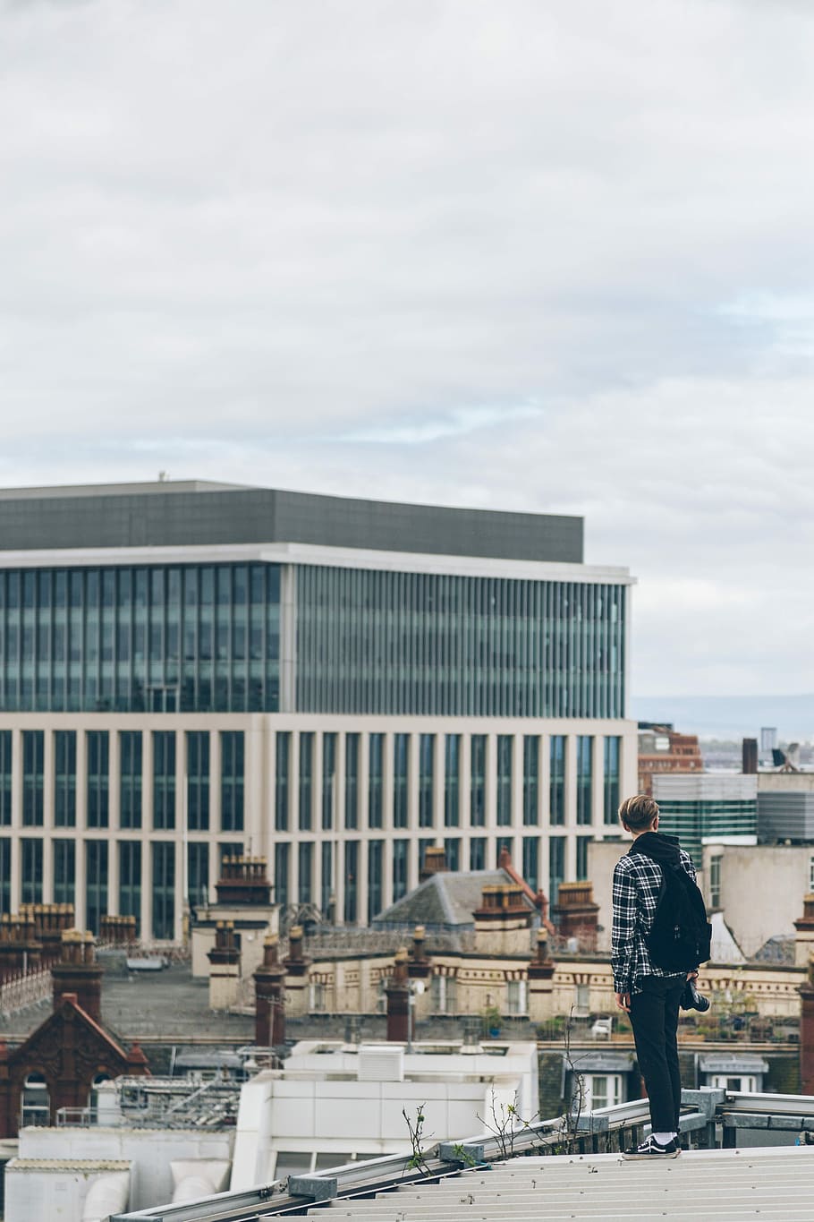 person with backpack standing on top of roof during daytime, man looking at white concrete building, HD wallpaper