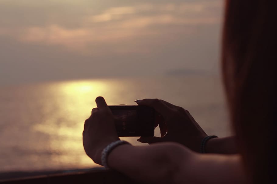 person holding camera taking photo of sea at sunset, photographing HD wallpaper