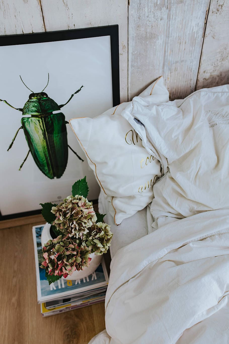 White bed sheets with a picture of a green beetle and a pot plant on a stack of magazines HD wallpaper
