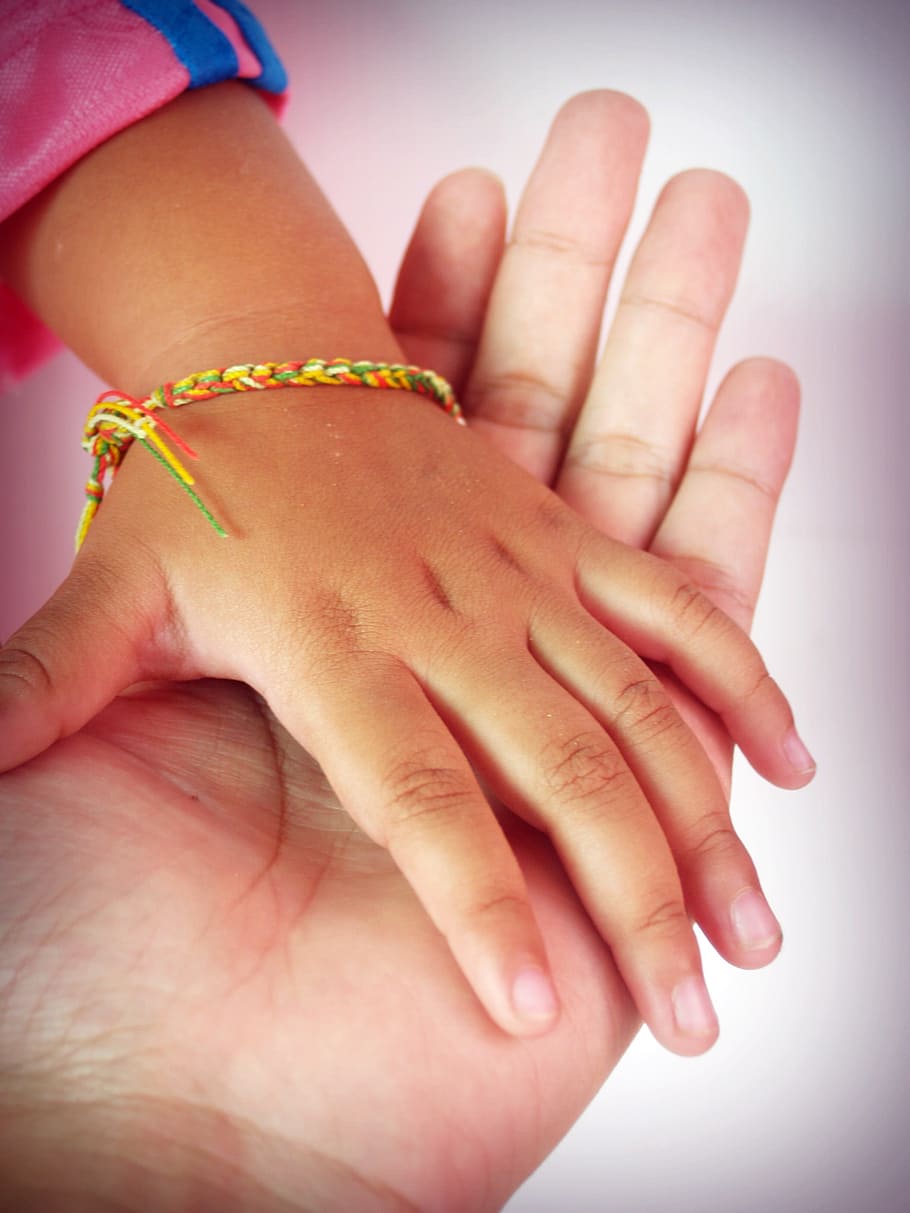 tilt lens photography of child's hand with bracelet over left palm of person HD wallpaper