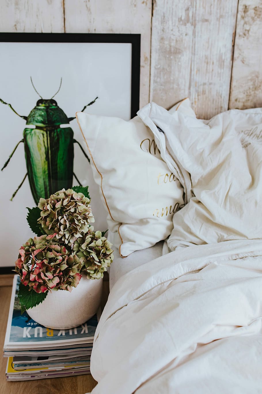 White bed sheets with a picture of a green beetle and a pot plant on a stack of magazines HD wallpaper