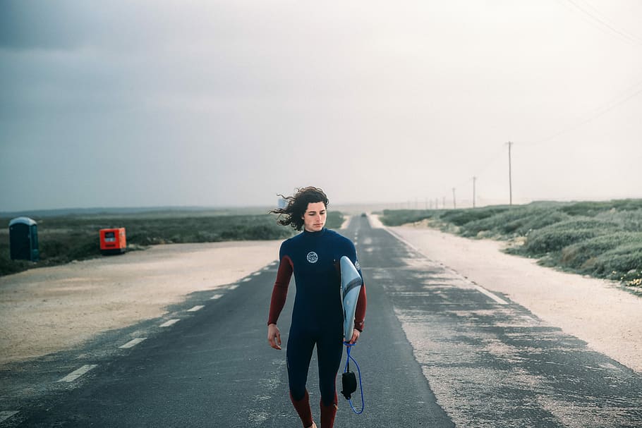 person walking on road, person carrying surfboard while standing on asphalt road HD wallpaper