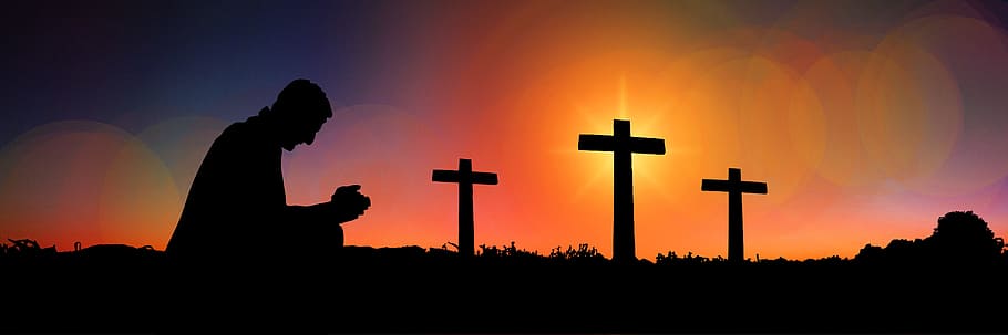 silhouette of man praying with three cross in background, sunset