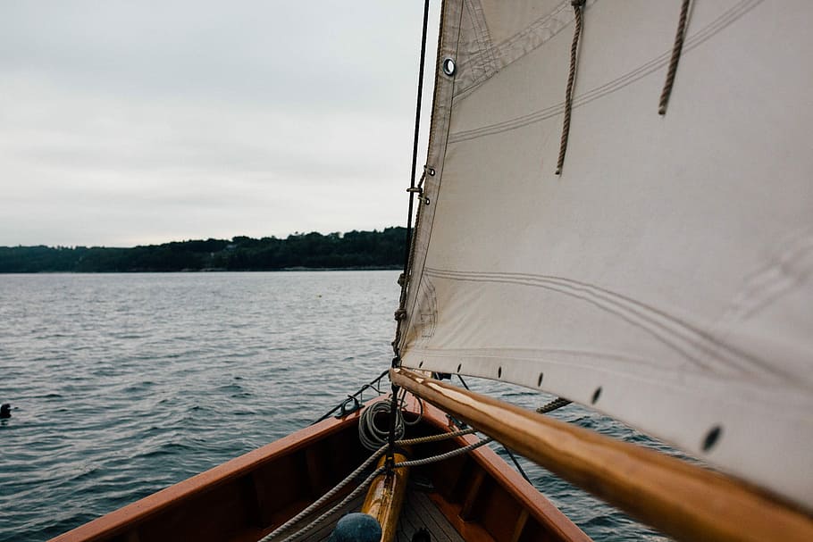 brown sailboat on ocean over silhouette of mountain under cloudy sky at daytime HD wallpaper