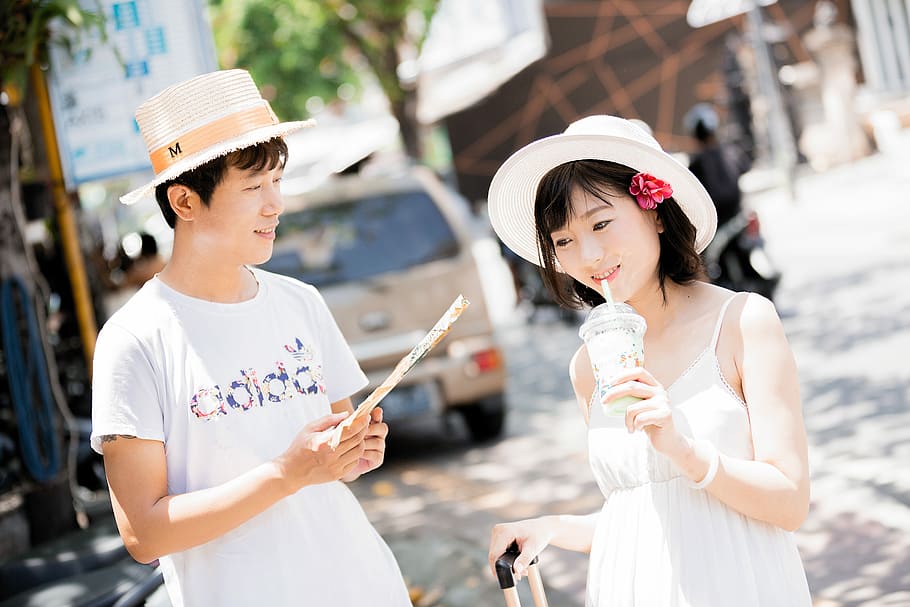 man and woman wearing hats holding disposable cups near vehicle during daytime, man holding hand fan beside woman wearing hat HD wallpaper