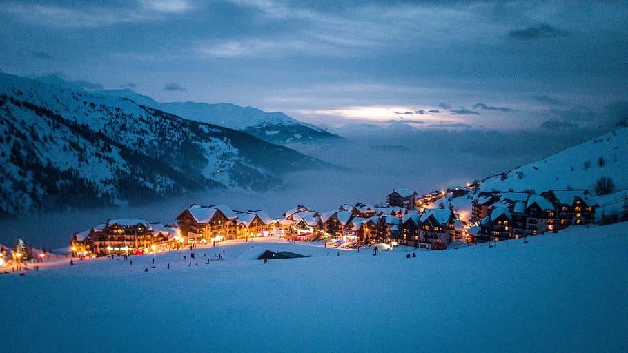 brown wooden houses surrounded by mountain taken at nighttime, low light photography of village in snowfield HD wallpaper