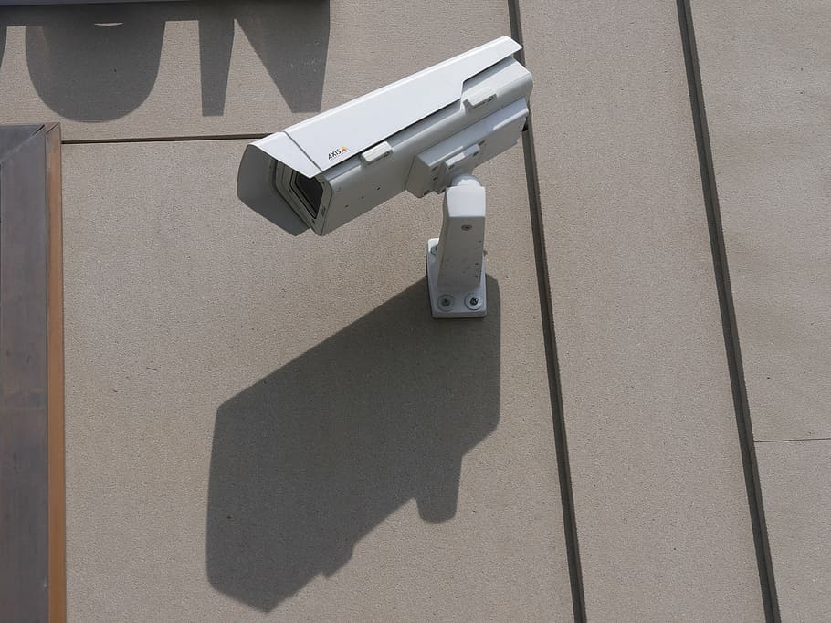 white surveillance camera hanging on wall at daytime, video surveillance