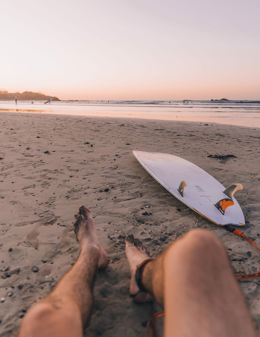 person sitting on seashore near surfboard in front sea, person lying on sand beach HD wallpaper