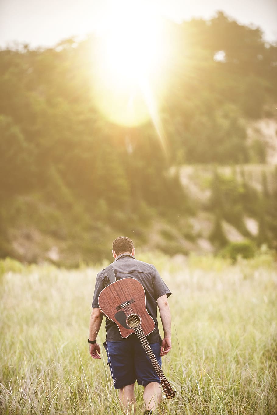 man walking on green grass field during daytime, man walking on green grass carrying guitar HD wallpaper