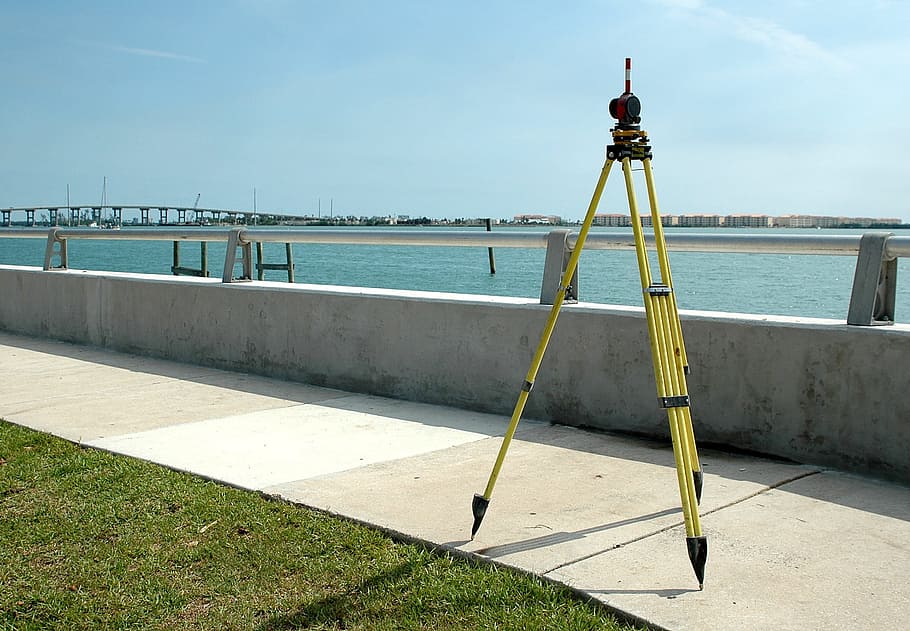 yellow steel tripod on concrete walk path outdoors, surveying
