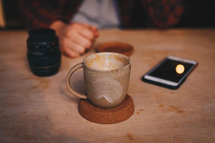 brown cup on brown saucer, focus photo of brown ceramic mug on table beside iPhone HD wallpaper