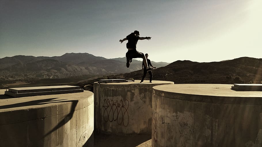 man jumping between two cylinder buldings, silhouette photo of man jumping between concrete container at daytime HD wallpaper
